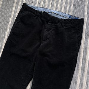 Puede incluir: Pantal&oacute;n de pana negro con una etiqueta amarilla y azul que dice "POLO RALPH LAUREN".
