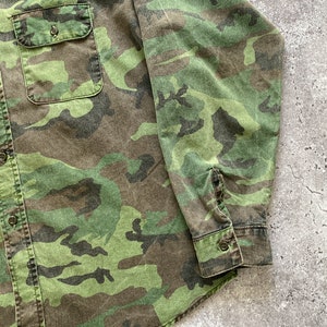 May include: A green, brown, and black camouflage long-sleeve shirt with a button-up front.