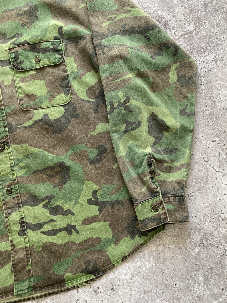 May include: A green, brown, and black camouflage long-sleeve shirt with a button-up front.