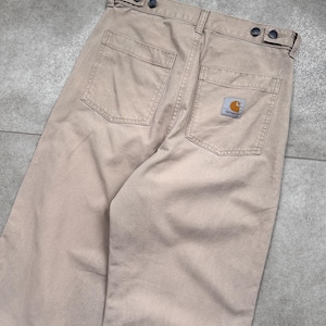 Puede incluir: Pantalones de trabajo color beige con dos bolsillos traseros y un peque&ntilde;o parche con el logotipo. Los pantalones tienen cierre de bot&oacute;n y un dise&ntilde;o de pierna recta. La tela parece duradera y adecuada para el trabajo o el uso casual.