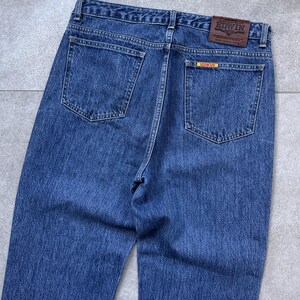 Pode incluir: Cal&ccedil;as de ganga azuis com dois bolsos traseiros e um remendo de couro castanho com a marca "EDWIN". As cal&ccedil;as de ganga t&ecirc;m um design cl&aacute;ssico de cinco bolsos e um corte reto. A ganga tem uma lavagem m&eacute;dia.