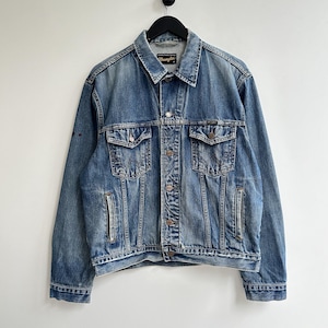 May include: A blue denim jacket with a Wrangler logo on the pocket. The jacket has a button closure and two pockets on the chest.
