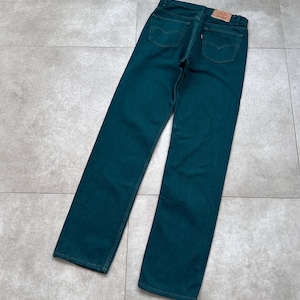 Op de afbeelding: Teal denim jeans met een klassiek ontwerp met vijf zakken. De jeans hebben een rechte pijp en een kleine, rechthoekige merkpatch op de achterste tailleband. De jeans liggen plat op een grijze tegelvloer.