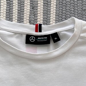 May include: White t-shirt with a black tag that says "AMG Petronas Motorsport" and "XL".