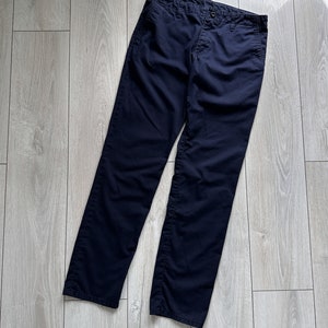 K&ouml;nnte beinhalten: Marineblaue Hose aus strapazierf&auml;higem Stoff. Die Hose hat einen Knopfverschluss und ein klassisches gerades Bein-Design. Das Kleidungsst&uuml;ck liegt flach auf einer hellen Holzoberfl&auml;che.