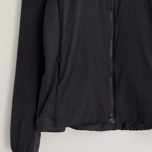 May include: Black athletic jacket with a full-length zipper. The jacket features a mesh panel on the side and a long sleeve. The jacket is made of a lightweight material.