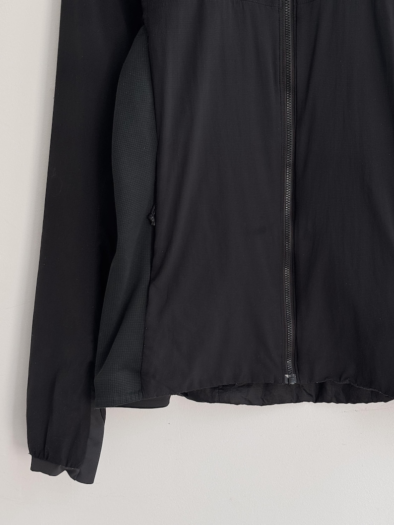 May include: Black athletic jacket with a full-length zipper. The jacket features a mesh panel on the side and a long sleeve. The jacket is made of a lightweight material.
