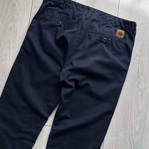 K&ouml;nnte beinhalten: Marineblaue Hose mit Knopfverschluss und zwei Ges&auml;&szlig;taschen. Ein braunes Lederpatch mit Logo ist hinten angen&auml;ht. Die Hose ist aus strapazierf&auml;higem Stoff gefertigt und f&uuml;r den Freizeitgebrauch geeignet.