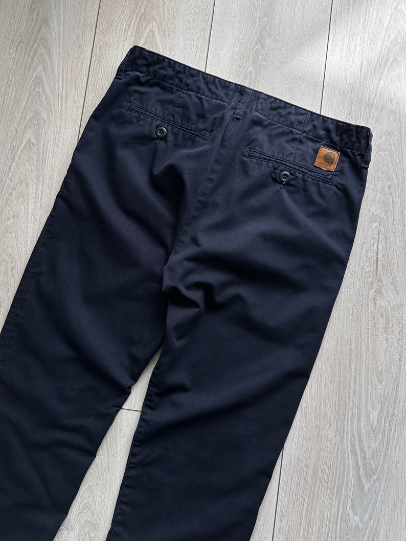 K&ouml;nnte beinhalten: Marineblaue Hose mit Knopfverschluss und zwei Ges&auml;&szlig;taschen. Ein braunes Lederpatch mit Logo ist hinten angen&auml;ht. Die Hose ist aus strapazierf&auml;higem Stoff gefertigt und f&uuml;r den Freizeitgebrauch geeignet.