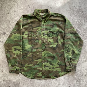 May include: A long-sleeved button-down shirt in a camouflage pattern. The shirt is made of a soft, cotton fabric and has a relaxed fit.