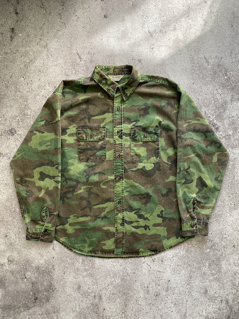 May include: A long-sleeved button-down shirt in a camouflage pattern. The shirt is made of a soft, cotton fabric and has a relaxed fit.