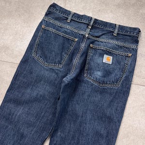 Puede incluir: Vaqueros de mezclilla azul oscuro con dos bolsillos traseros y un peque&ntilde;o parche cuadrado con el logotipo. Los vaqueros tienen un dise&ntilde;o cl&aacute;sico de cinco bolsillos y un corte recto. Las costuras son de color dorado en contraste.