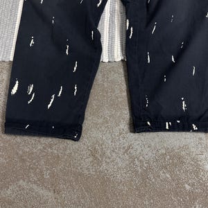 Puede incluir: Pantalones azul marino oscuro con un patr&oacute;n abstracto blanco de pinceladas. Los pantalones est&aacute;n doblados en el dobladillo. El fondo incluye una alfombra a rayas grises y blancas y una superficie de hormig&oacute;n gris.