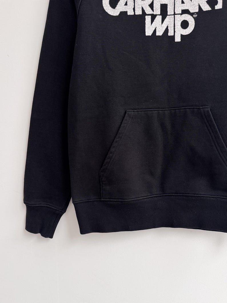 May include: Black hoodie with a kangaroo pocket and ribbed cuffs and hem. The white text "CARHARTT WIP" is printed across the chest. The hoodie is made of a soft, comfortable material.