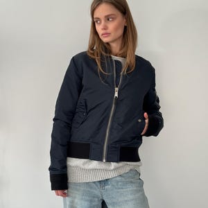 May include: A dark blue bomber jacket with a zip fastening and a black ribbed knit collar, cuffs, and waistband.