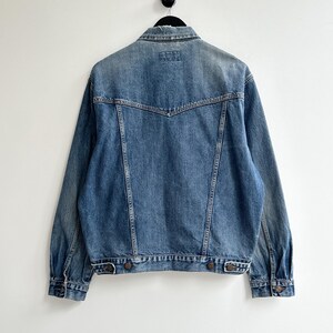 May include: A blue denim jacket with a pointed collar, long sleeves, and button closure. The jacket has a faded look and is made of a soft, comfortable material.