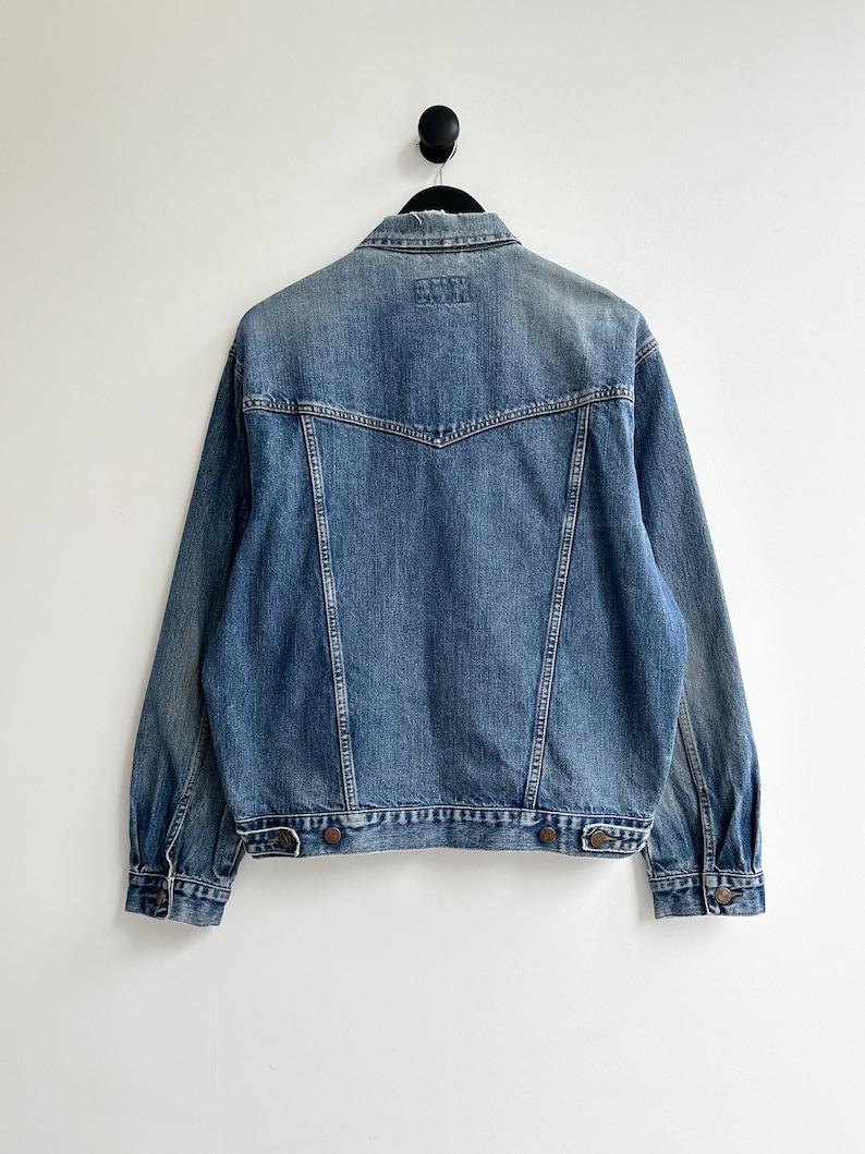 May include: A blue denim jacket with a pointed collar, long sleeves, and button closure. The jacket has a faded look and is made of a soft, comfortable material.