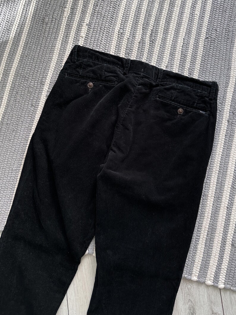Puede incluir: Pantal&oacute;n de pana negro de pierna recta. El pantal&oacute;n tiene dos bolsillos traseros con cierre de bot&oacute;n.