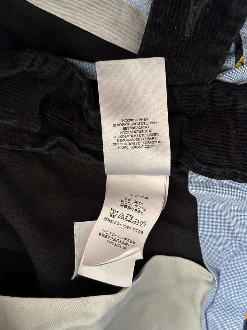 Puede incluir: Una camisa a rayas negras y azules con cuello blanco y una etiqueta blanca con instrucciones de cuidado en varios idiomas. La etiqueta incluye el texto "Исключением декоративной отделки / Без украсата/ &Alpha;&pi;&omicron;&kappa;&lambda;&epsilon;&iota;&sigma;&tau;&iota;&kappa;ή &alpha;&pi;&omicron; &delta;&iota;&alpha;&kappa;ό&sigma;&mu;&eta;&sigma;&eta;/Utelukker Dekorasjon/Enbart Dekoration/Dekorasyon Hari&ccedil; Krome Ozdob".