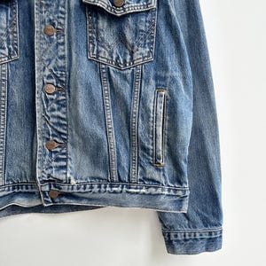 May include: A blue denim jacket with a button closure and a Wrangler logo on the pocket.