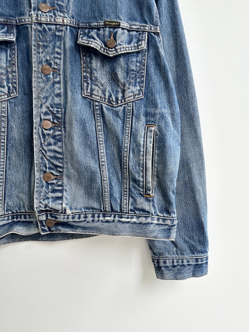 May include: A blue denim jacket with a button closure and a Wrangler logo on the pocket.