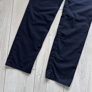 K&ouml;nnte beinhalten: Eine marineblaue Hose mit geradem Bein. Der dunkelblaue Stoff wird auf einer hellen Holzoptik-Oberfl&auml;che pr&auml;sentiert. Das Bild zeigt den unteren Teil der Hose, einschlie&szlig;lich S&auml;ume und N&auml;hte.