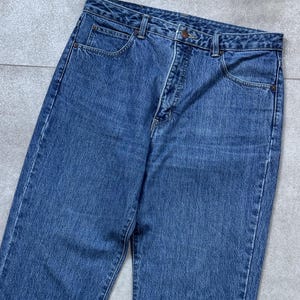 Pode incluir: Um par de cal&ccedil;as de ganga azuis. As cal&ccedil;as de ganga t&ecirc;m um design cl&aacute;ssico de cinco bolsos, um fecho de bot&atilde;o e z&iacute;per e presilhas para cinto. A ganga tem uma lavagem m&eacute;dia e um aspeto ligeiramente desbotado, sugerindo um estilo vintage.