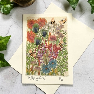 May include: A card with a colorful illustration of a garden with flowers, leaves, and bees. The text "In the Garden" is written at the bottom of the card.