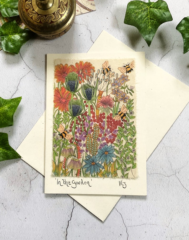 May include: A card with a colorful illustration of a garden with flowers, leaves, and bees. The text "In the Garden" is written at the bottom of the card.