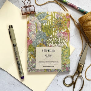 May include: A small notebook with a colourful floral design on the cover. The cover features a title that reads "Kitty Jane Wild Garden Pen and Ink by Kitty Cooke". The text below the title reads "Kitty Cooke is a North Devon illustrator who creates intricate boho designs - often inspired by Indian ethnic art, florals and mandalas kittyjanedesigns.co.uk".