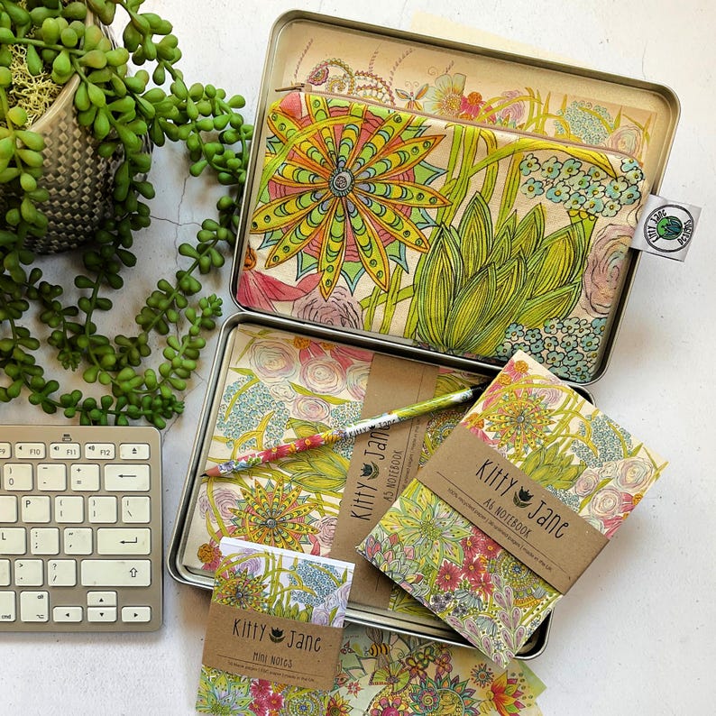 May include: A set of colourful floral patterned stationery items in a tin box. The set includes a notebook, a mini notepad, a pencil, and a pouch. The items are all decorated with a vibrant floral design.