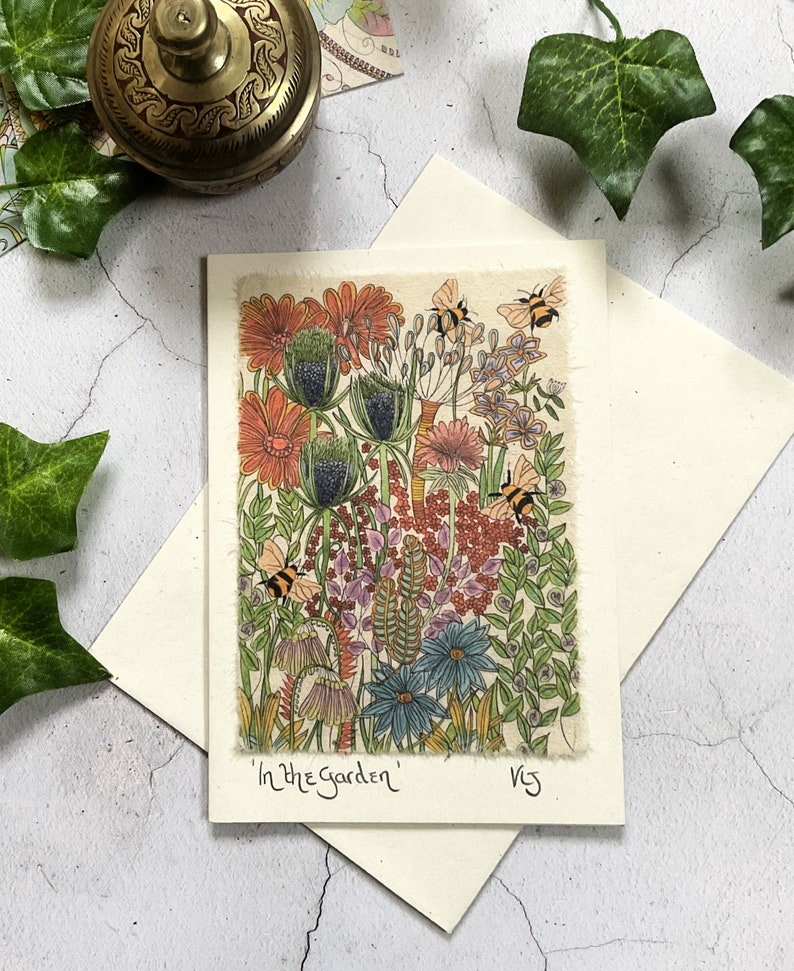 May include: A card with a colorful illustration of a garden with flowers, leaves, and bees. The text "In the Garden" is written at the bottom of the card.