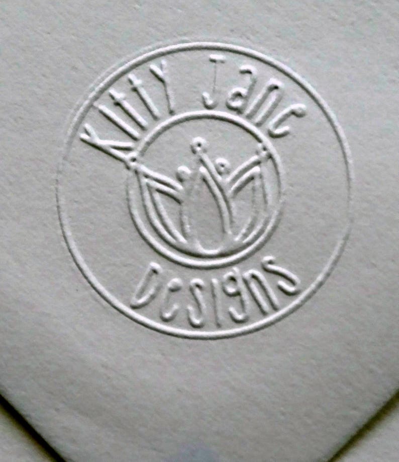 May include: A white embossed circle with the text "Kitty Jane Designs" and a stylized image of three people with their arms raised.