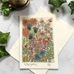 May include: A card with a colorful illustration of a garden with flowers, leaves, and bees. The text "In the Garden" is written at the bottom of the card.
