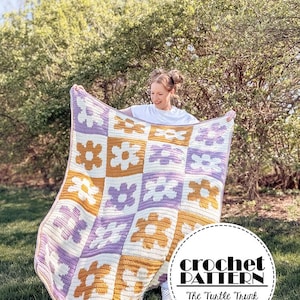 Peut inclure: Une couverture au crochet faite à la main avec un motif floral en blanc, lavande et jaune moutarde. La couverture est tenue par une personne portant un t-shirt blanc. Le motif au crochet est visible. Le texte "crochet PATTERN The Turtle Trunk" est en bas à droite.