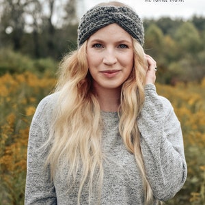 May include: A woman wearing a gray knit headband with a twisted design. The headband is worn over her forehead and hair. The woman is wearing a gray sweater and has long blonde hair. The background is a field of yellow flowers.