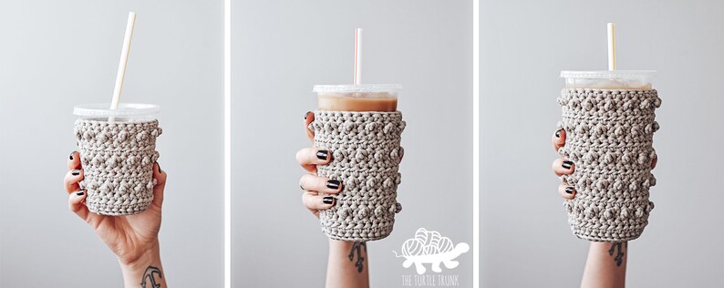 May include: A beige crocheted cup cozy with a textured bobble stitch pattern. The cozy is on a clear plastic cup with a straw.