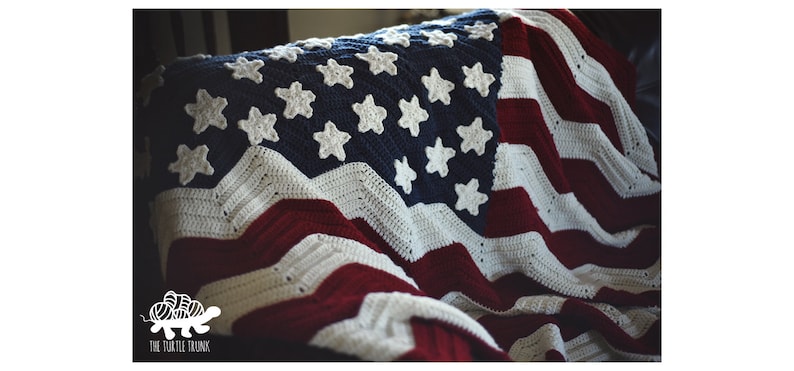 May include: A crocheted American flag blanket in red, white, and blue with white stars on a blue field. The blanket is folded and draped over a chair.