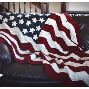 May include: A crocheted American flag blanket in red, white, and blue, draped over a brown leather couch.