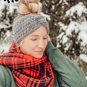 May include: A woman wearing a gray crocheted headband and a red and black plaid scarf. The background is a snowy forest.