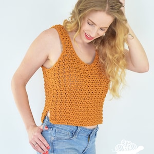 May include: A crocheted tank top in a burnt orange color with a loose, open stitch pattern. The top has a scoop neck and a slightly cropped length. The model is wearing the top with ripped denim jeans.