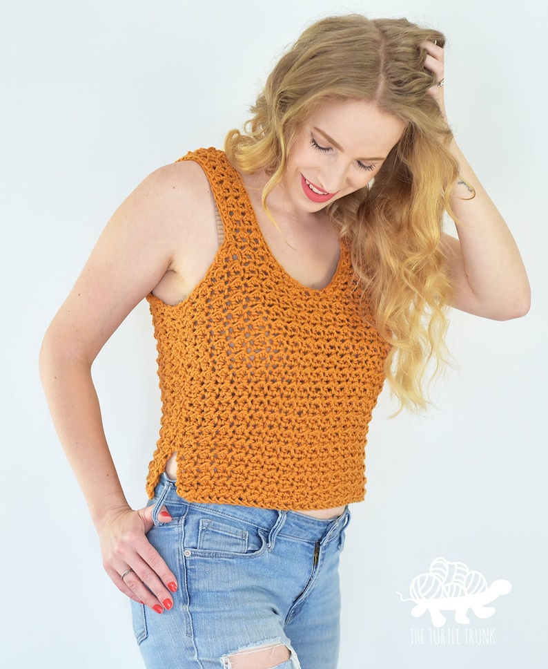 May include: A crocheted tank top in a burnt orange color with a loose, open stitch pattern. The top has a scoop neck and a slightly cropped length. The model is wearing the top with ripped denim jeans.
