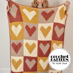 May include: A crochet blanket with a patchwork design featuring hearts in shades of red, yellow, white, and brown. The blanket is held up by a person, and the text "crochet pattern" and "The Turtle Thunk" is visible in the lower right corner.