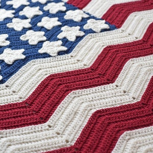 May include: A crocheted American flag blanket with red, white, and blue stripes and a blue field of white stars. The blanket is made with a chevron stitch pattern.