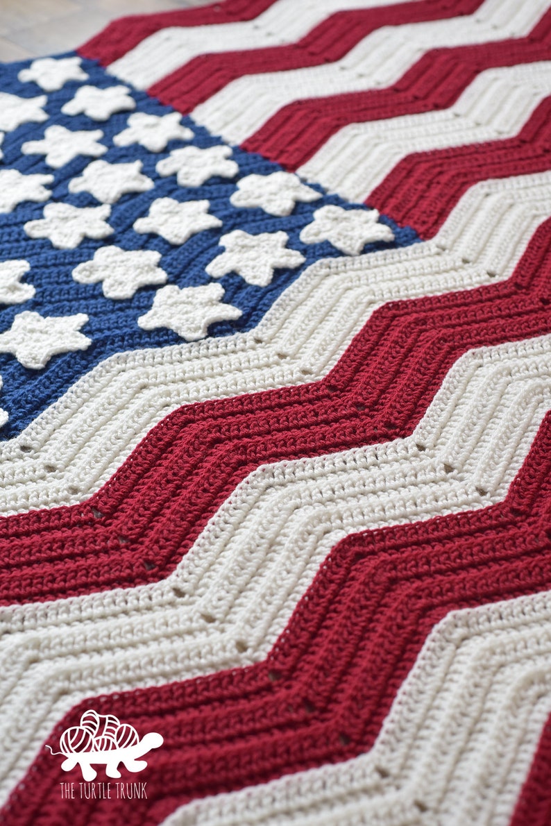May include: A crocheted American flag blanket with red, white, and blue stripes and a blue field of white stars. The blanket is made with a chevron stitch pattern.