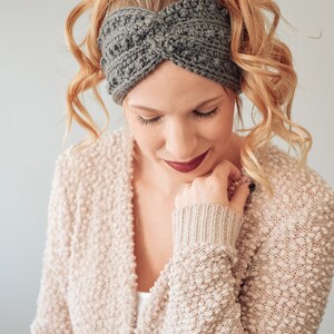 May include: A woman with long, curly blonde hair is wearing a gray crocheted headband. The headband is twisted and has a textured design. The woman is wearing a light beige cardigan with a textured pattern.