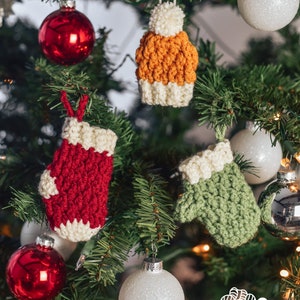 May include: A Christmas tree decorated with crocheted ornaments, including a red mitten, a green mitten, and an orange and white hat. The tree is also decorated with red and white ornaments.