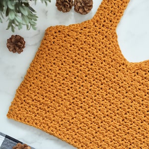 May include: A mustard yellow crochet top with a wide, scoop neck and thin straps. The top is made with a textured stitch and has a cropped length.