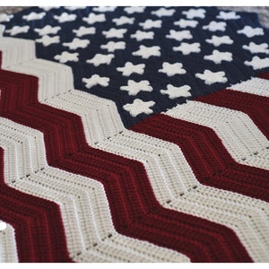 May include: A crocheted American flag blanket with red, white, and blue stripes and stars. The blanket is made with a chevron stitch pattern.