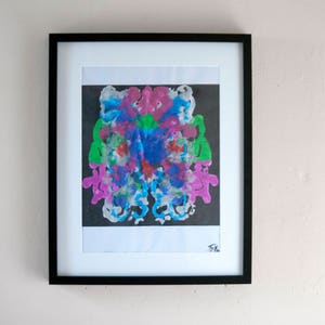 Può includere: Un dipinto astratto incorniciato con un designo simmetrico di schizzi di vernice rosa, blu, verde e bianca su uno sfondo nero. Il dipinto è firmato "FK".